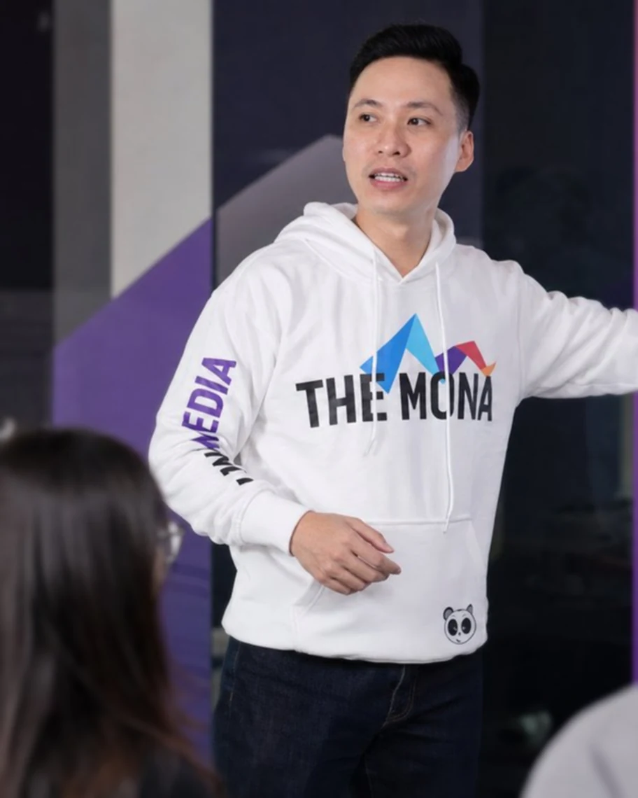 Nhân sự MONA Media mặc áo THE MONA đứng trao đổi cùng đồng nghiệp trong buổi họp nhanh đầu ngày