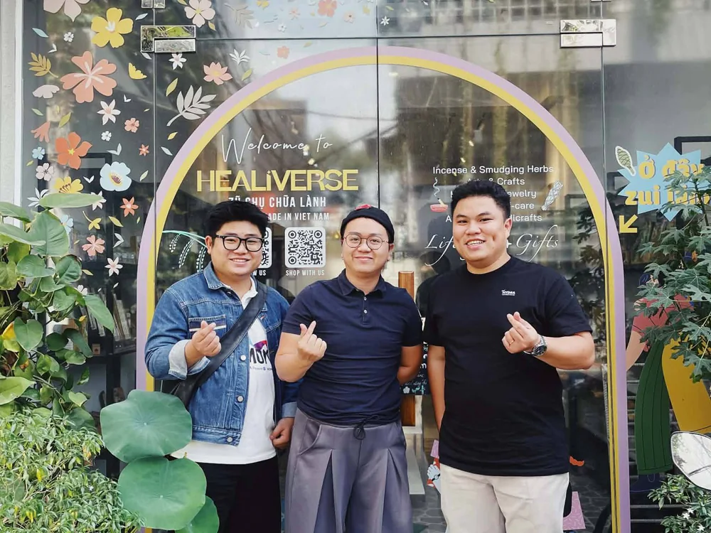 Nhân sự MONA chụp cùng hai người trước cửa kính cửa hàng Healiverse