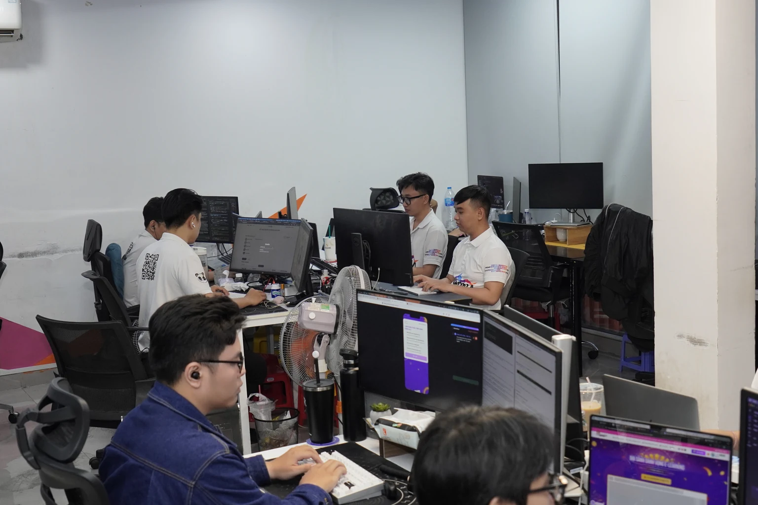 Sàn làm việc của đội kỹ thuật MONA, nhiều màn hình, nhiều người đang code