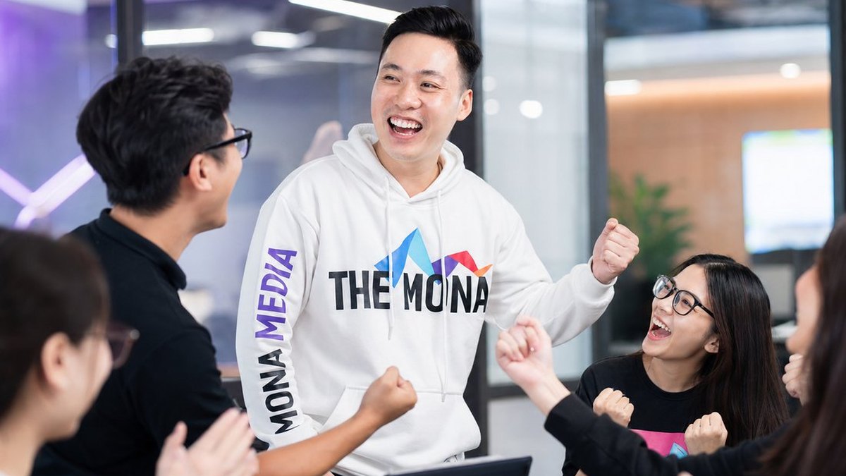 Đội ngũ MONA mặc hoodie THE MONA cùng làm việc và ăn mừng tại văn phòng